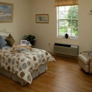 A cozy bedroom with a neatly made bed, featuring a decorative comforter, a window offering natural light, and comfortable seating.