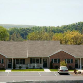 A row of residential buildings with a parking lot in the foreground and a wooded landscape in the background.