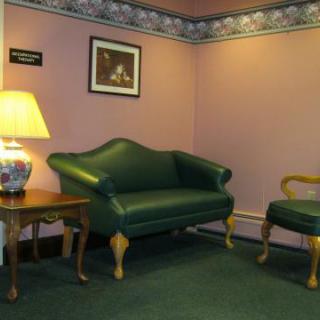 A cozy lounge area with a green sofa and chair, accompanied by a side table with a lamp.