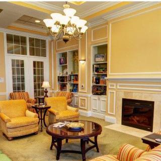 A cozy living room with elegant yellow walls, comfortable seating, and a fireplace, complemented by built-in bookshelves and overhead lighting.