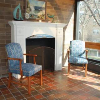 A cozy interior with two chairs flanking a decorative fireplace, sunlit through a large window.