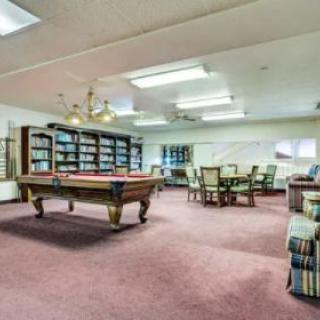 A spacious recreational room featuring a pool table and library shelves, with ample seating and warm lighting.