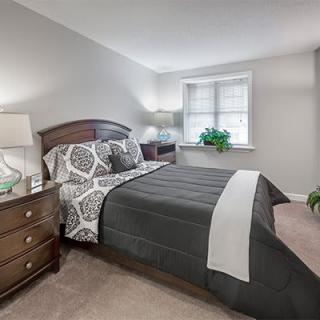 A cozy bedroom with a neatly made bed, nightstand, and potted plant by the window.