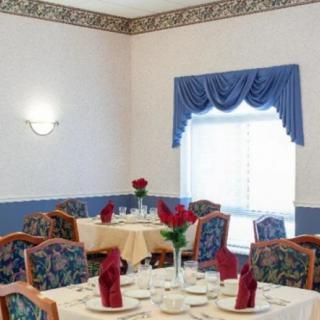 A neatly set dining room with tables adorned with red napkins and flowers, featuring blue curtains and patterned chairs.