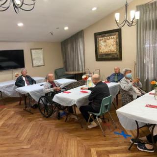 A group of seniors gathered in a cozy indoor setting, engaging in conversation at their tables.