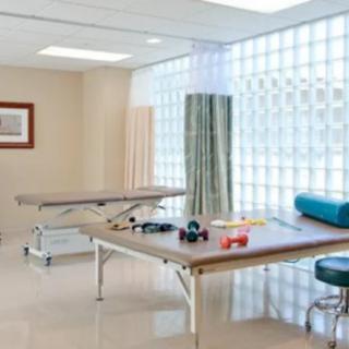 A physical therapy treatment room equipped with exercise equipment and tables.