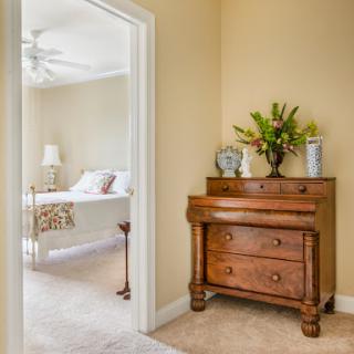 A cozy corner of a bedroom showcasing a wooden dresser adorned with flowers, leading to a softly lit sleeping area.