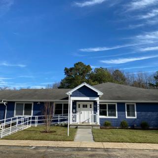 A single-story blue house with a front porch and ramp set against a bright blue sky.