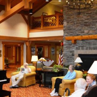 A cozy lounge area in a retirement home with seniors seated around, featuring comfortable furniture and a stone fireplace.