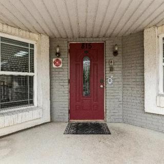 A welcoming red front door on a brick house, flanked by two windows and adorned with a decorative wreath.