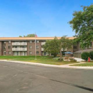 A residential apartment building with surrounding trees and a road in front, captured on a clear day.