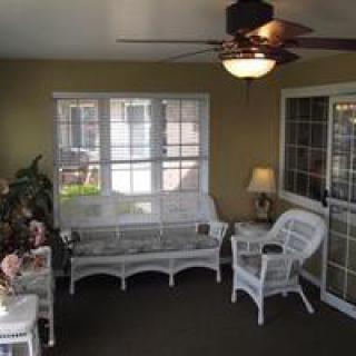 A cozy sunroom featuring wicker furniture and a ceiling fan, with natural light streaming in through the windows.