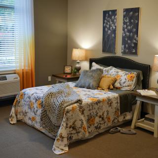 A cozy bedroom with stylish decor, featuring a bed adorned with a patterned comforter, two bedside lamps, and wall art.