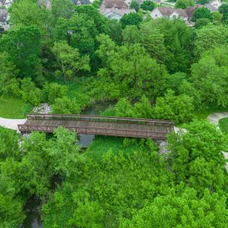 Aerial view of a park featuring a wooden bridge surrounded by lush greenery and winding pathways.
