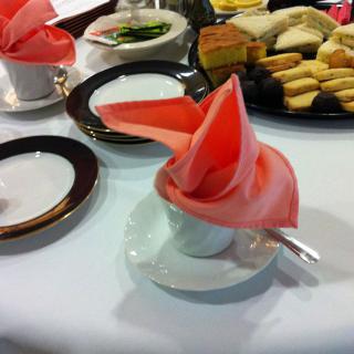 A table set with tea cups adorned with folded napkins, accompanied by an assortment of pastries and snacks.