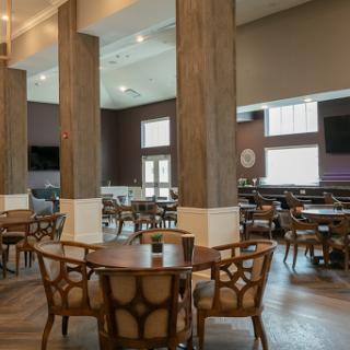 A spacious and modern dining area featuring wooden tables and chairs, complemented by large windows that allow ample natural light.