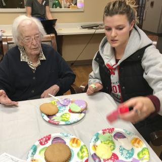 An elderly woman and a young woman are decorating cookies together.