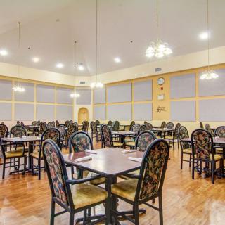 An empty dining room with neatly arranged tables and chairs, illuminated by overhead lighting.