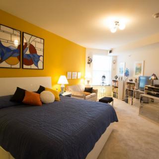 A modern, cozy bedroom featuring a yellow accent wall, artwork above the bed, and comfortable furniture.