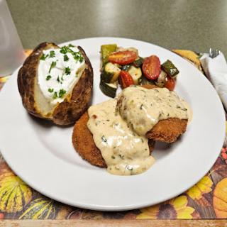 A delicious dinner plate featuring baked potato with sour cream, fried items topped with gravy, and a side of mixed vegetables.