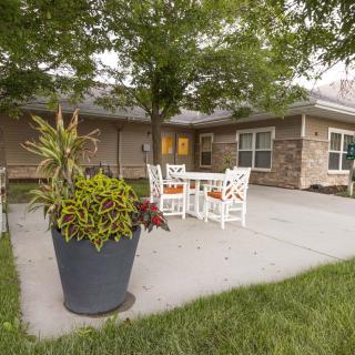 A cozy outdoor patio with white furniture, surrounded by greenery and a large potted plant.