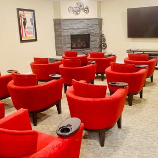 A cozy home theater with vibrant red chairs arranged in front of a large screen and fireplace.