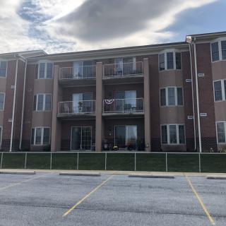 A three-story apartment building with balconies and a parking lot in front.