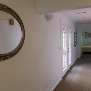 A bright hallway with a decorative mirror and glass doors leading to another room.