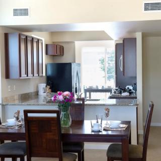 A modern open-layout kitchen with a dining area featuring wooden furniture and a vase of flowers.