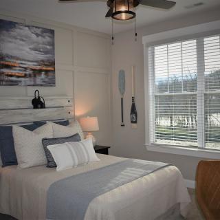 A cozy bedroom featuring a nautical-themed decor with a comfortable bed, wall art, paddle decorations, and a large window with blinds.