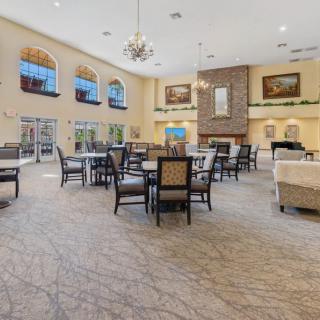 A spacious and elegant dining area with multiple tables and a chandelier, featuring large windows and a fireplace.