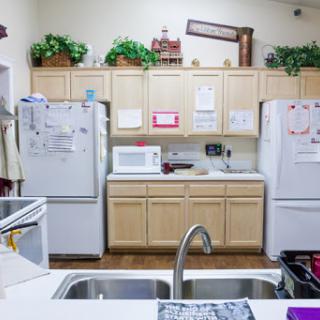 A cozy kitchen featuring wooden cabinets, two refrigerators, a microwave, and decorative plants.