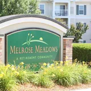 Sign for Melrose Meadows Retirement Community in front of landscaped greenery and residential buildings.