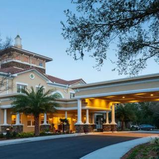 A well-lit building entrance with palm trees and a driveway at dusk.