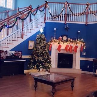 A festive living room decorated for Christmas with a tree, stockings on the fireplace, and garlands on the staircase.