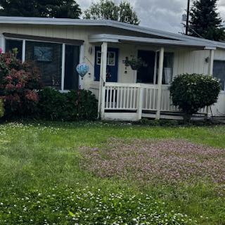 A cozy house with a welcoming porch, surrounded by lush greenery and a cloudy sky.