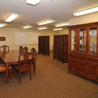 A conference room with a large wooden meeting table and chairs, surrounded by cabinets and shelves.