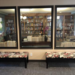 Interior view of a library with bookshelves and benches visible through large windows.