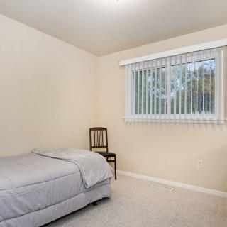 A minimalist bedroom with a single bed, chair, and window with blinds.