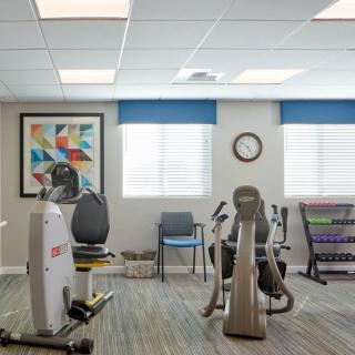A well-lit gym room with exercise equipment, chairs, and decorative artwork on the wall.
