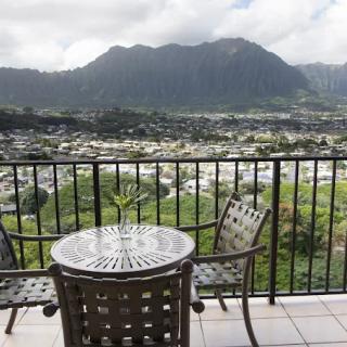 A scenic view from a balcony, featuring mountains in the background and a table with chairs in the foreground.