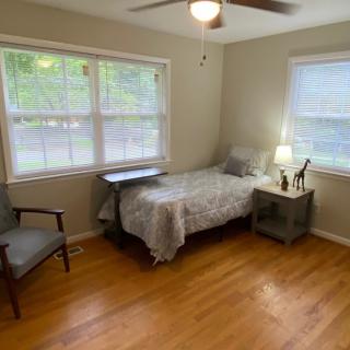 A cozy bedroom with a single bed, chair, and nightstand by the window.