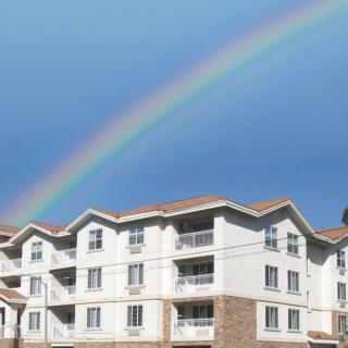 A vibrant rainbow arcs over a modern apartment building under a clear blue sky.