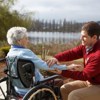 A caregiver assisting an elderly woman in a wheelchair by the lakeside.