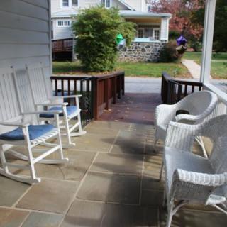 A cozy front porch with white rocking and wicker chairs overlooking a suburban neighborhood.
