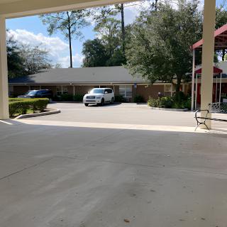 A small parking lot with parked cars in front of a building surrounded by trees on a sunny day.