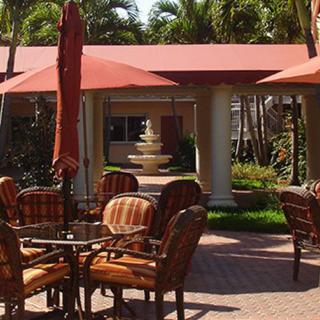 An outdoor patio area with tables, chairs, and umbrellas, leading to a garden with a fountain.