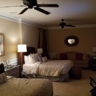A spacious hotel bedroom featuring two beds, a comfortable couch, and ceiling fans, adorned with warm neutral tones.