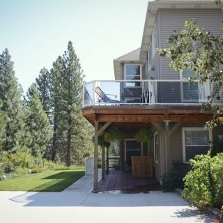 A house with a deck overlooking a lush green lawn and surrounded by trees.