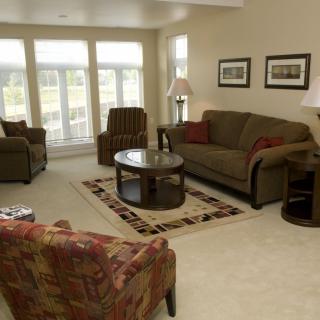 A cozy living room with sofas, chairs, a coffee table, and large windows.